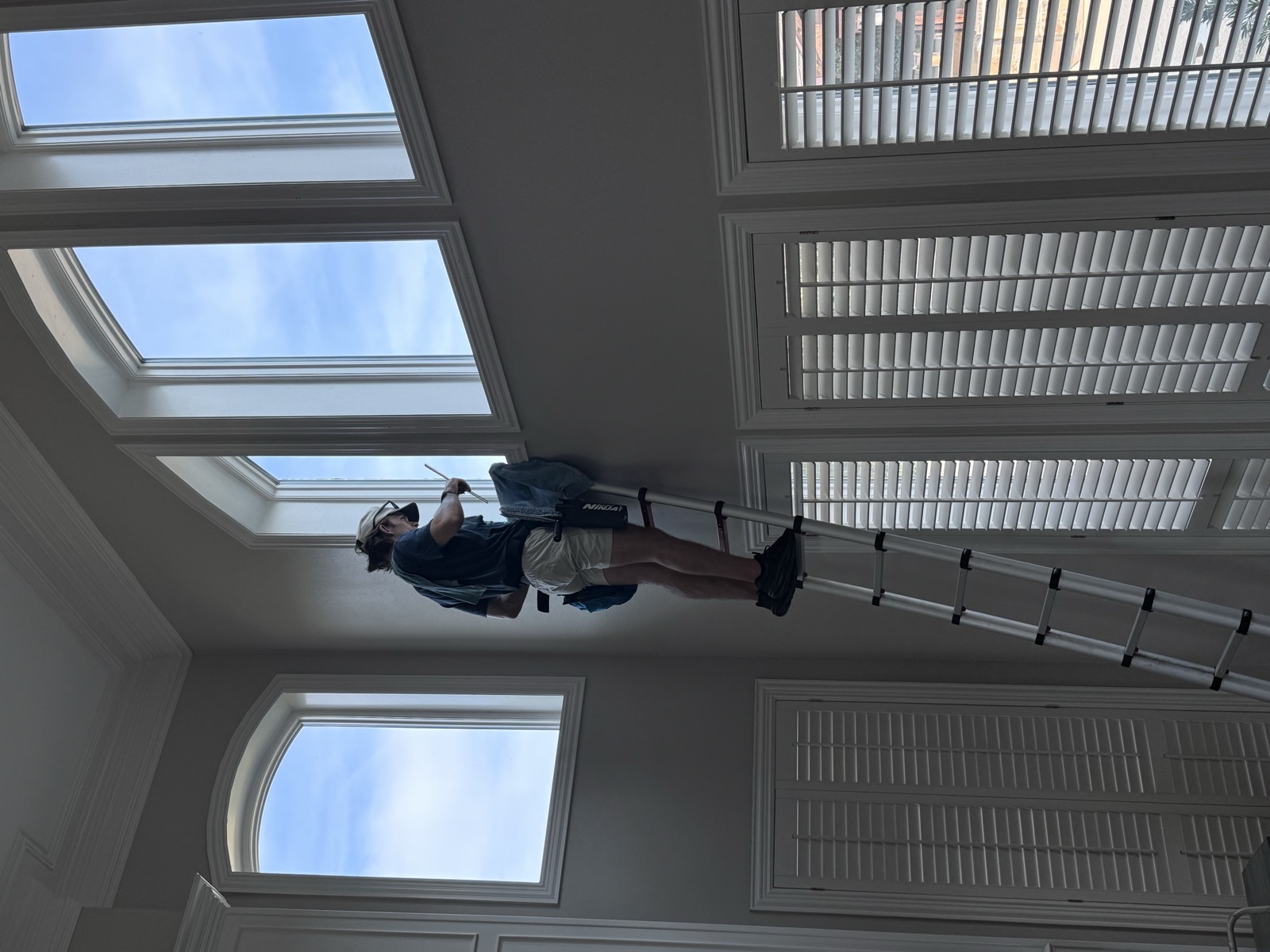GlowGrids technician cleaning tall interior windows in a two-story home